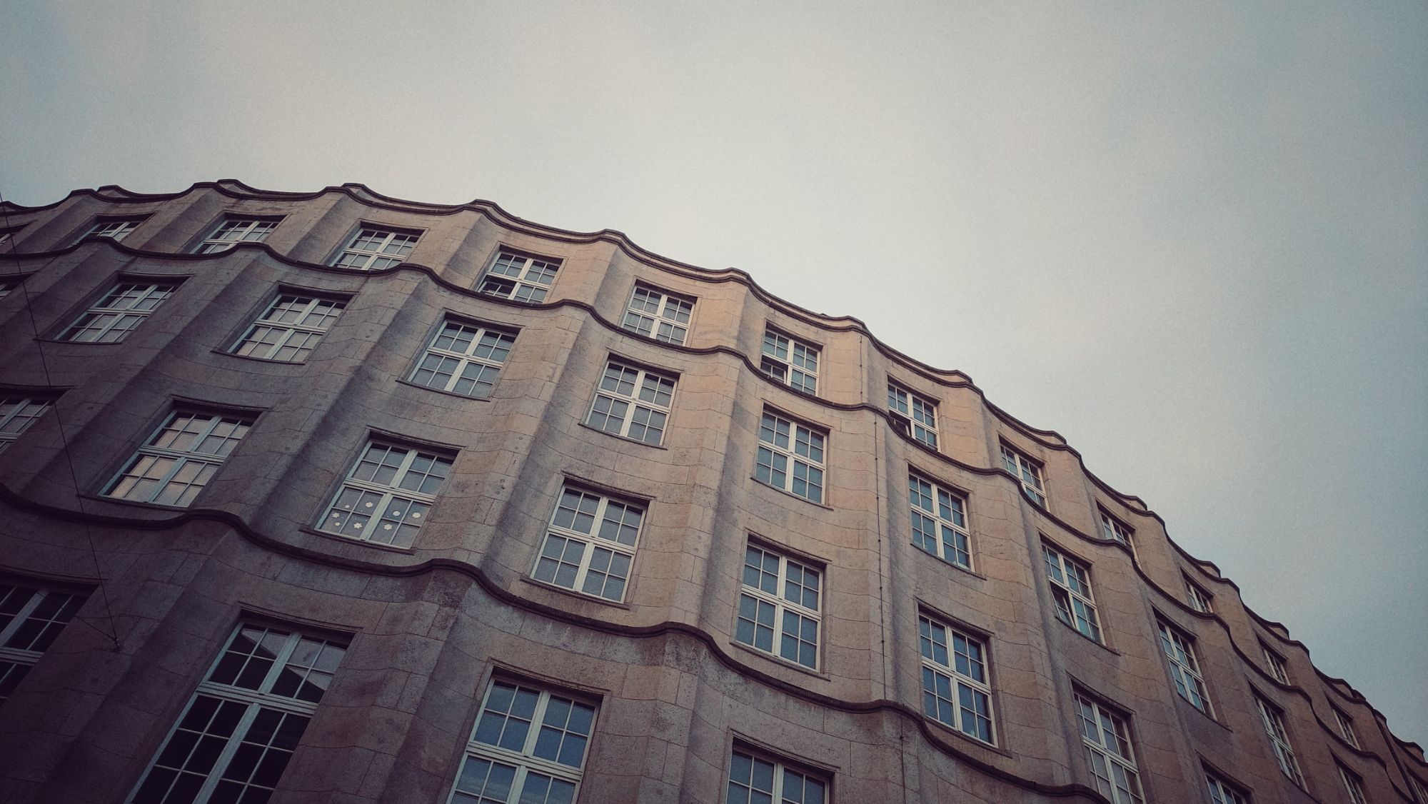 A little light of sunrise on an expressionist building facade, four floors of rectangular windows, a rounded structure with an almost organic flow.