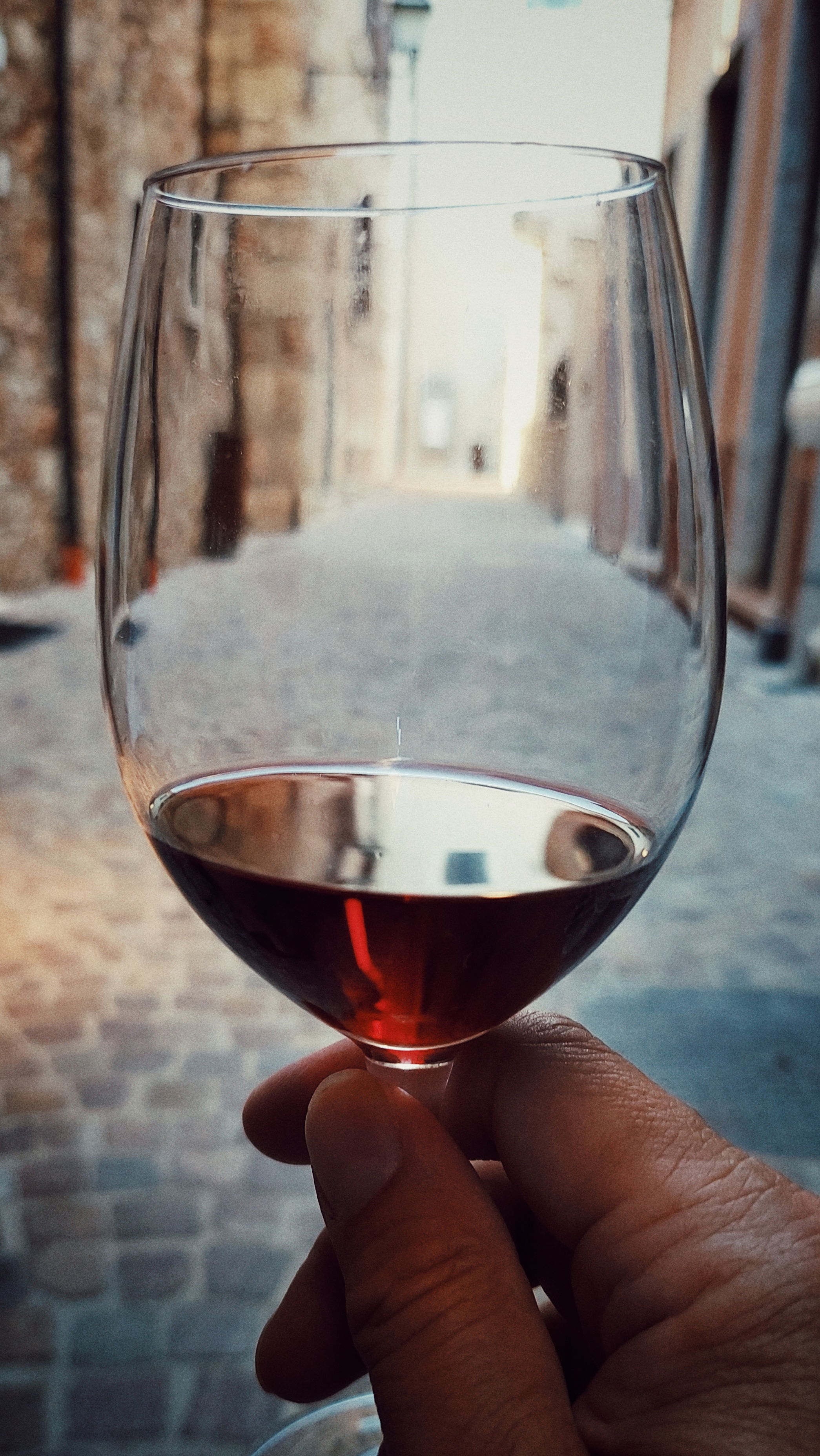 My hand holding a glass of red wine in a small narrow alley.