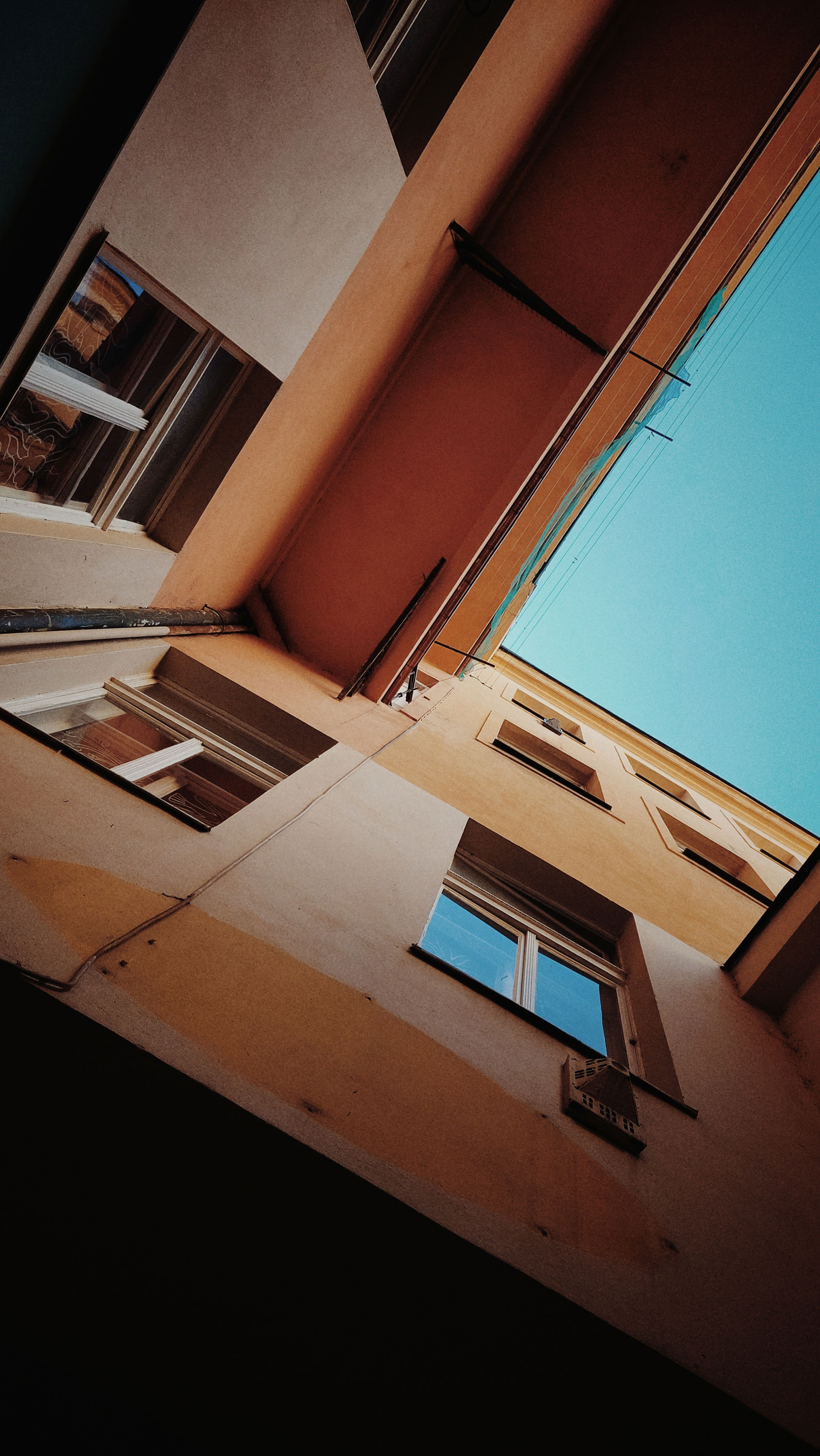 Looking up an older facade of houses, from a narrow backyard. Windows and blue sky above.