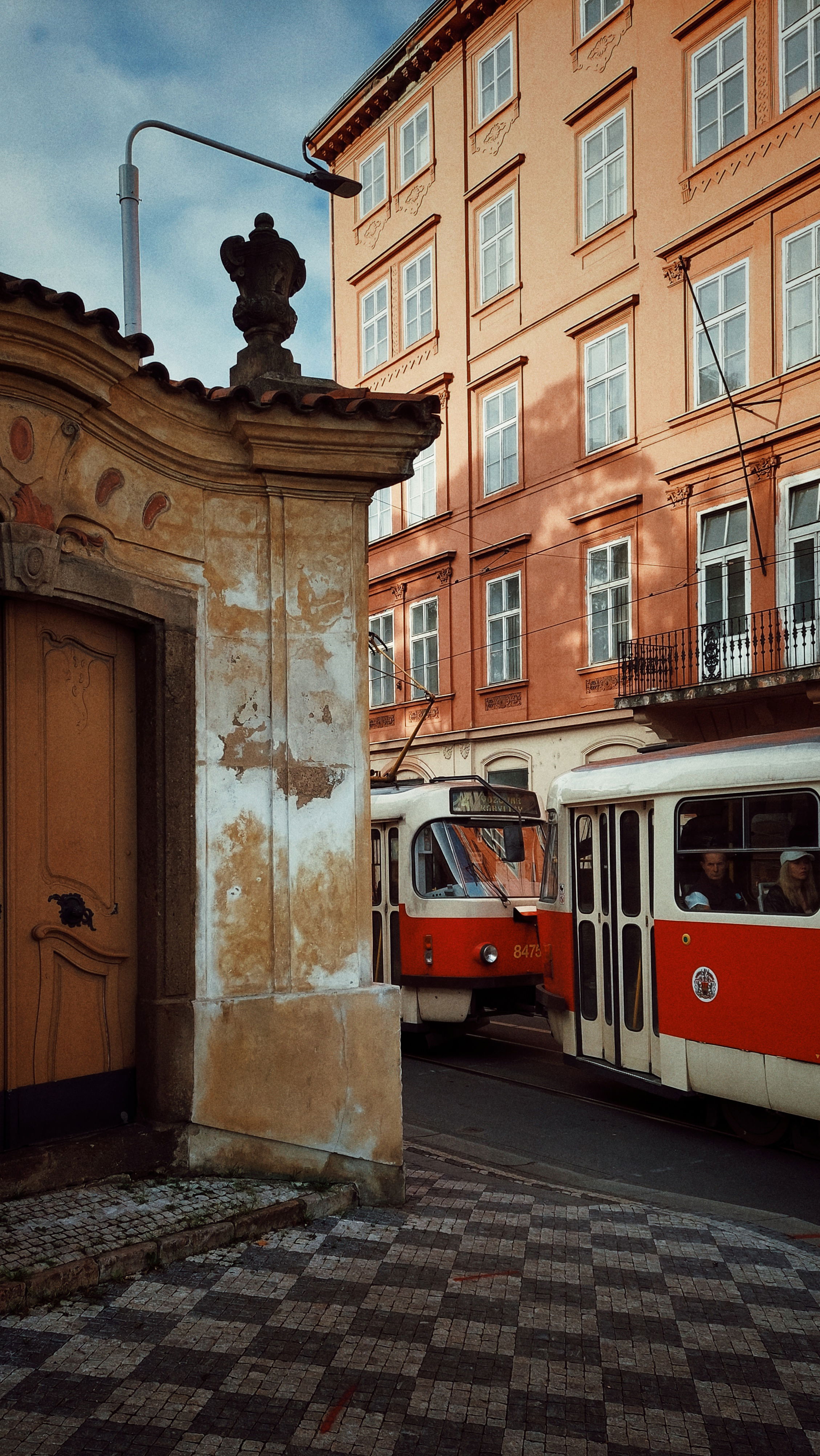 An old Tatra tram between an old monastery door and a slightly newer brick building.