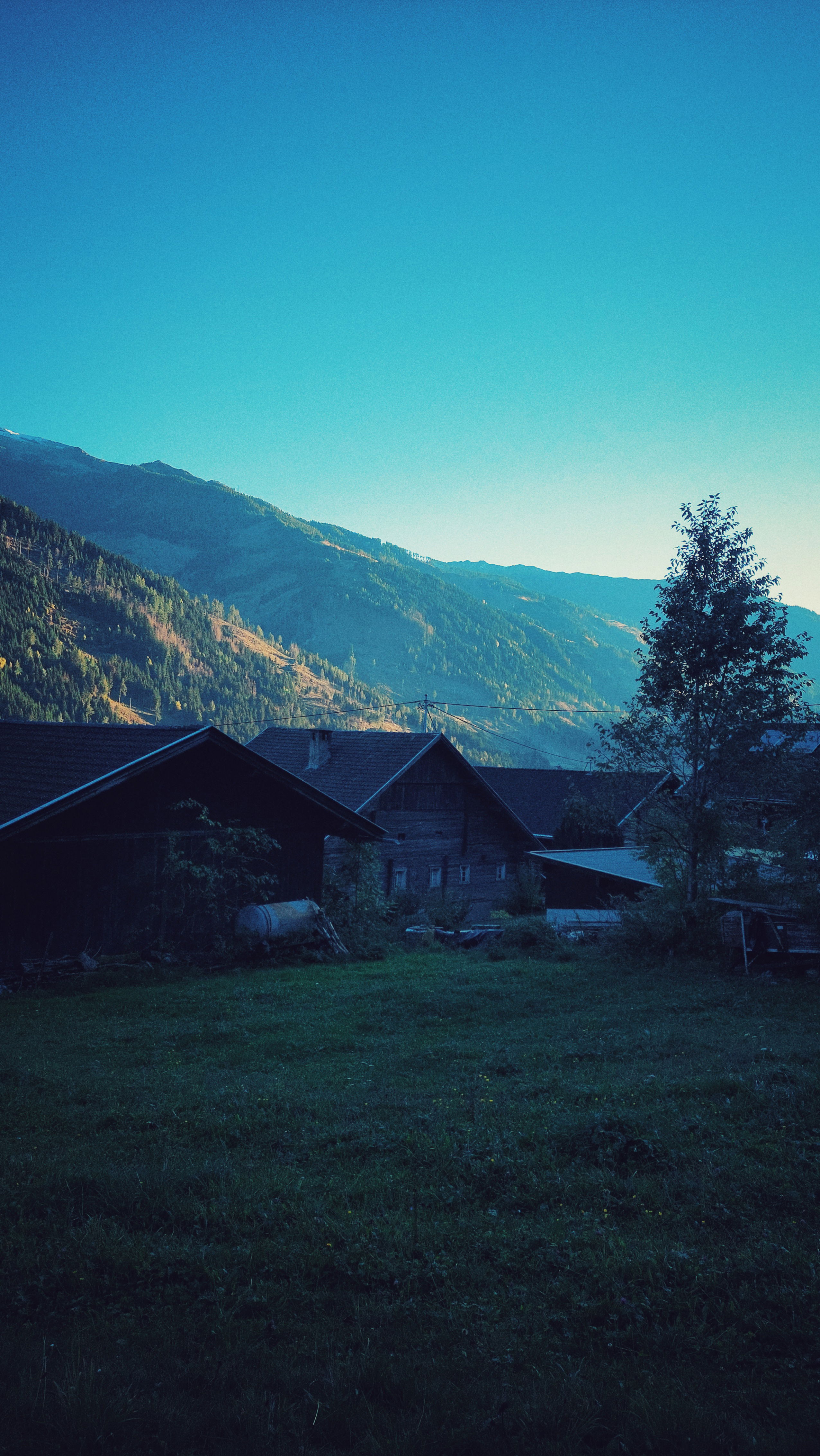 Mountains and sunset in a valley. An old farm and a meadow in front. 