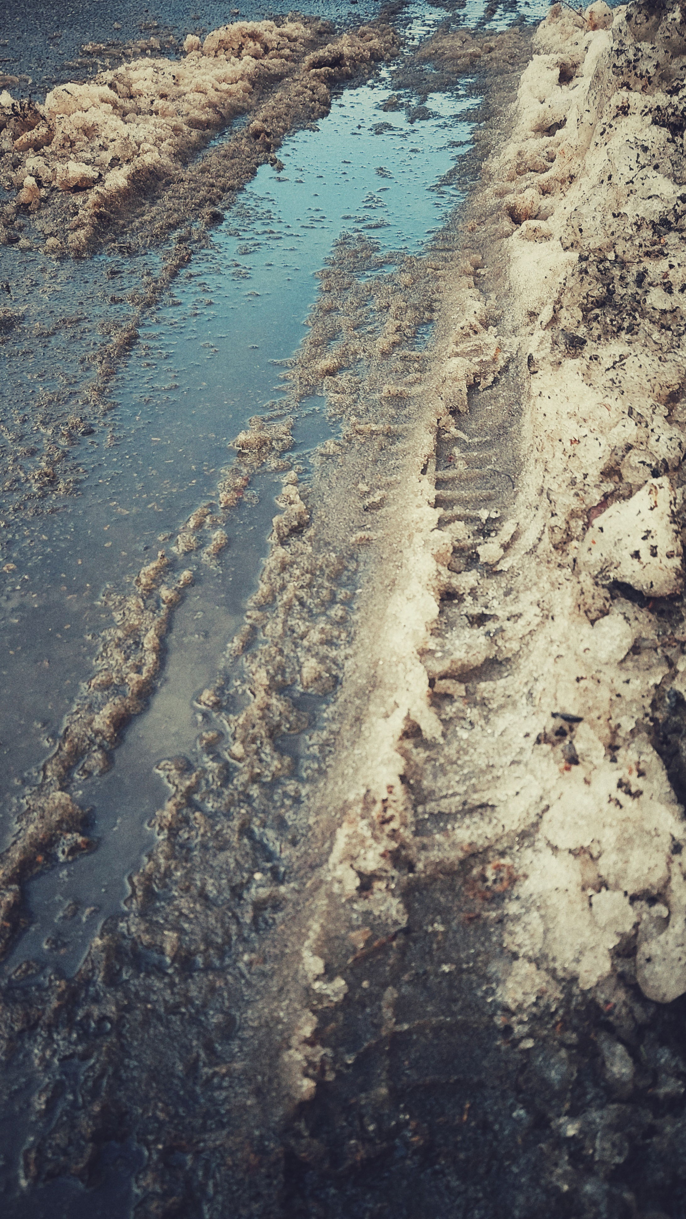 Remainders of snow on a concrete surface. A rough pile on the left, some footsteps and water in between. Car traces. And a reflection of blue sky in the back.