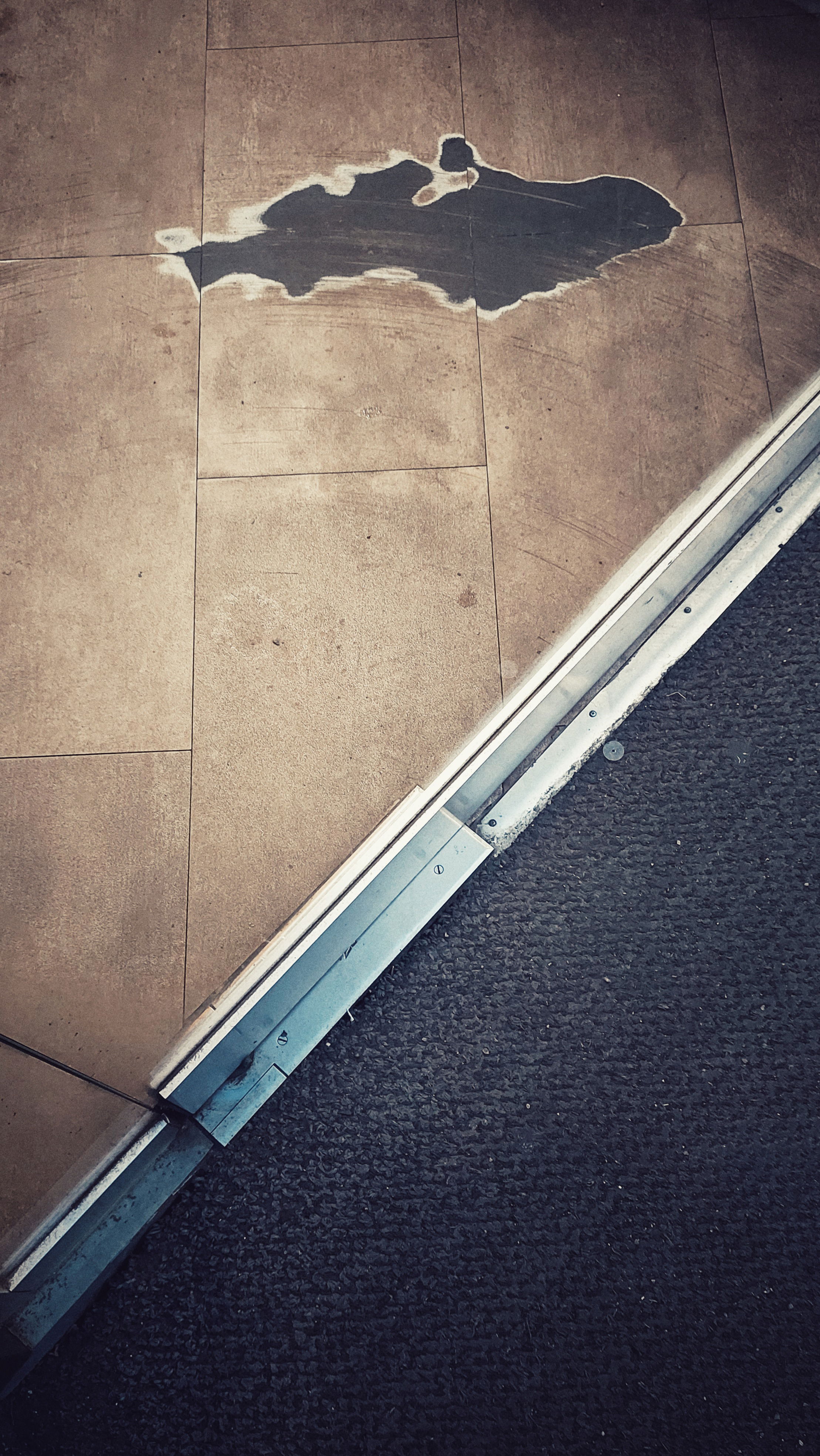 A shot of two kinds of floor separated by a metal rail. In the upper part there's a defect reminding of a country on a map.