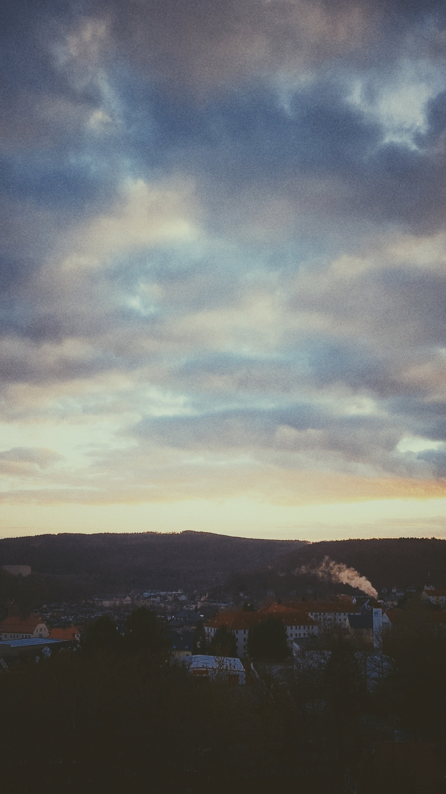 Sunset sky above hills and city roofs. 