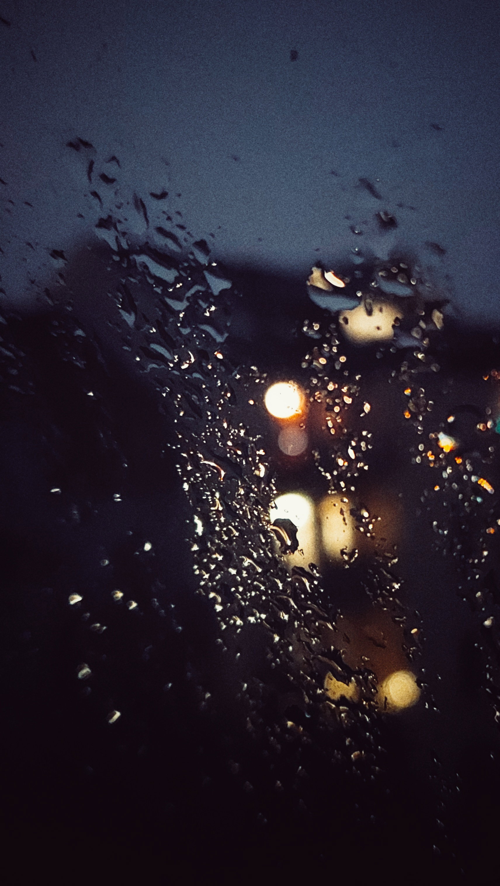 City houses behind a windowpane. Dense raindrops on the glass.