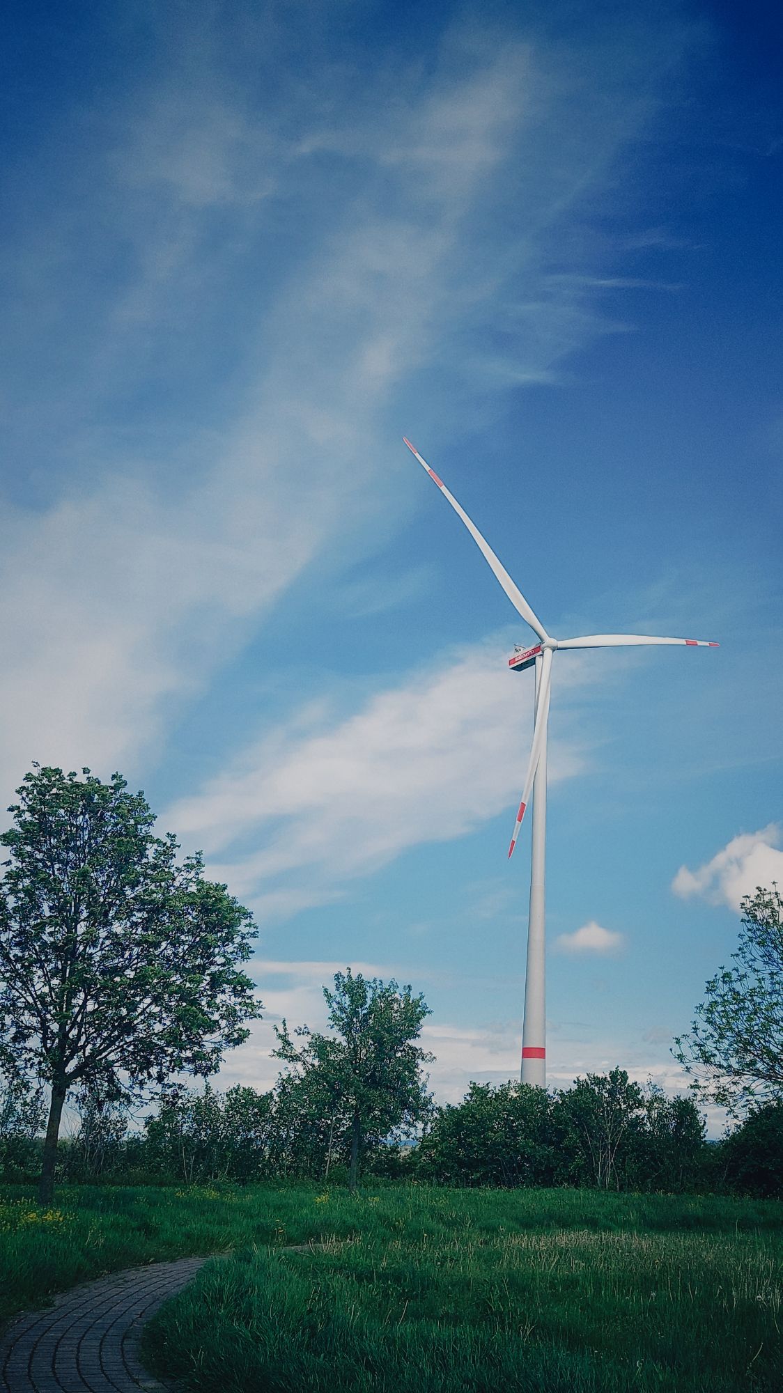 A wind turbine in front of a blue and white sky.