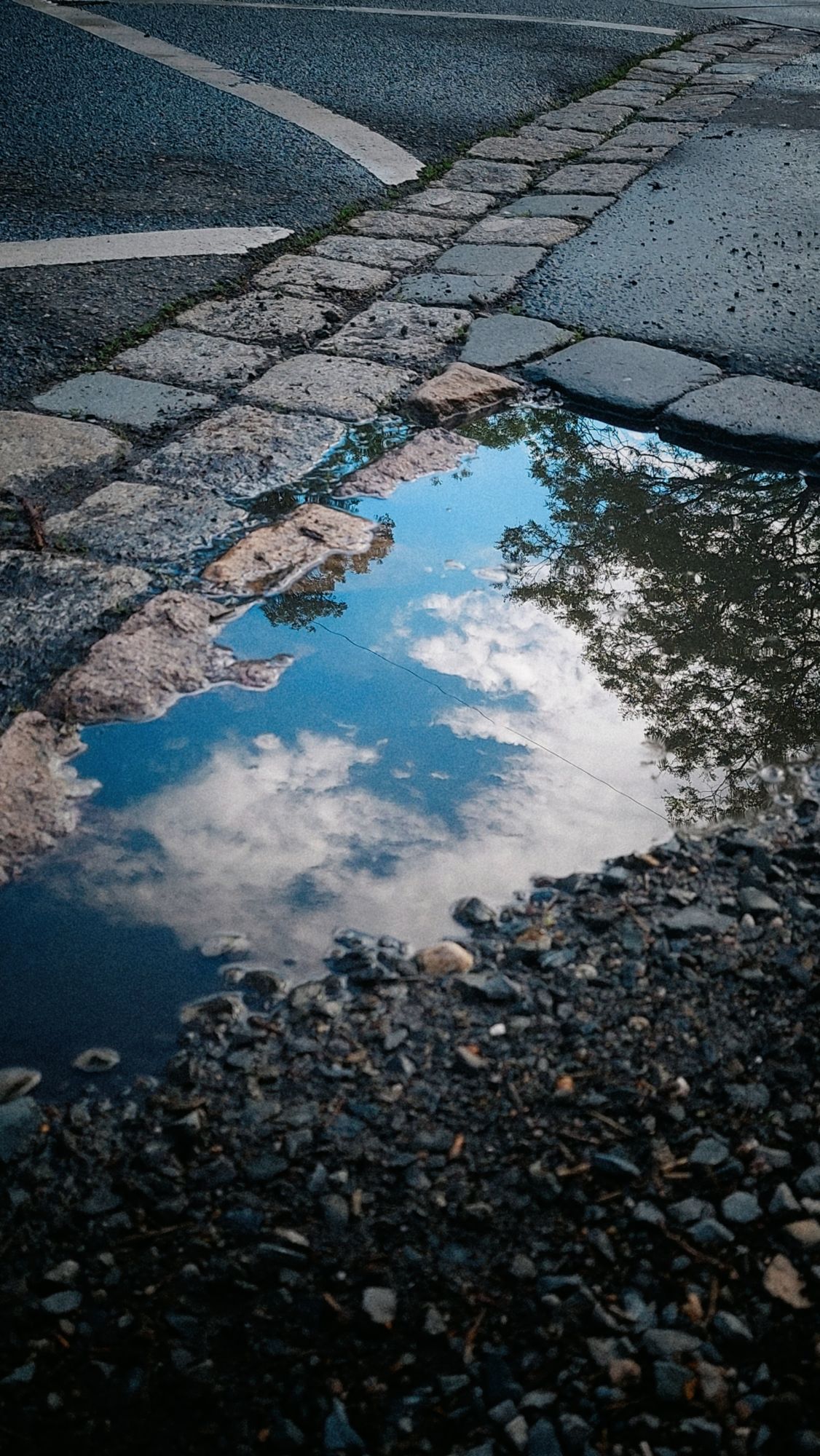 A blue and cloudy sky in a puddle near a crossroad.