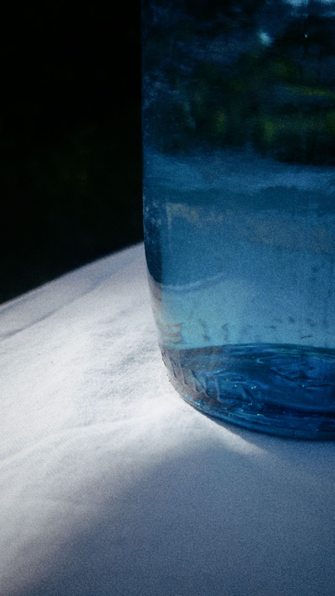 A blue bottle containing a transparent liquid, placed on a white tablecloth.