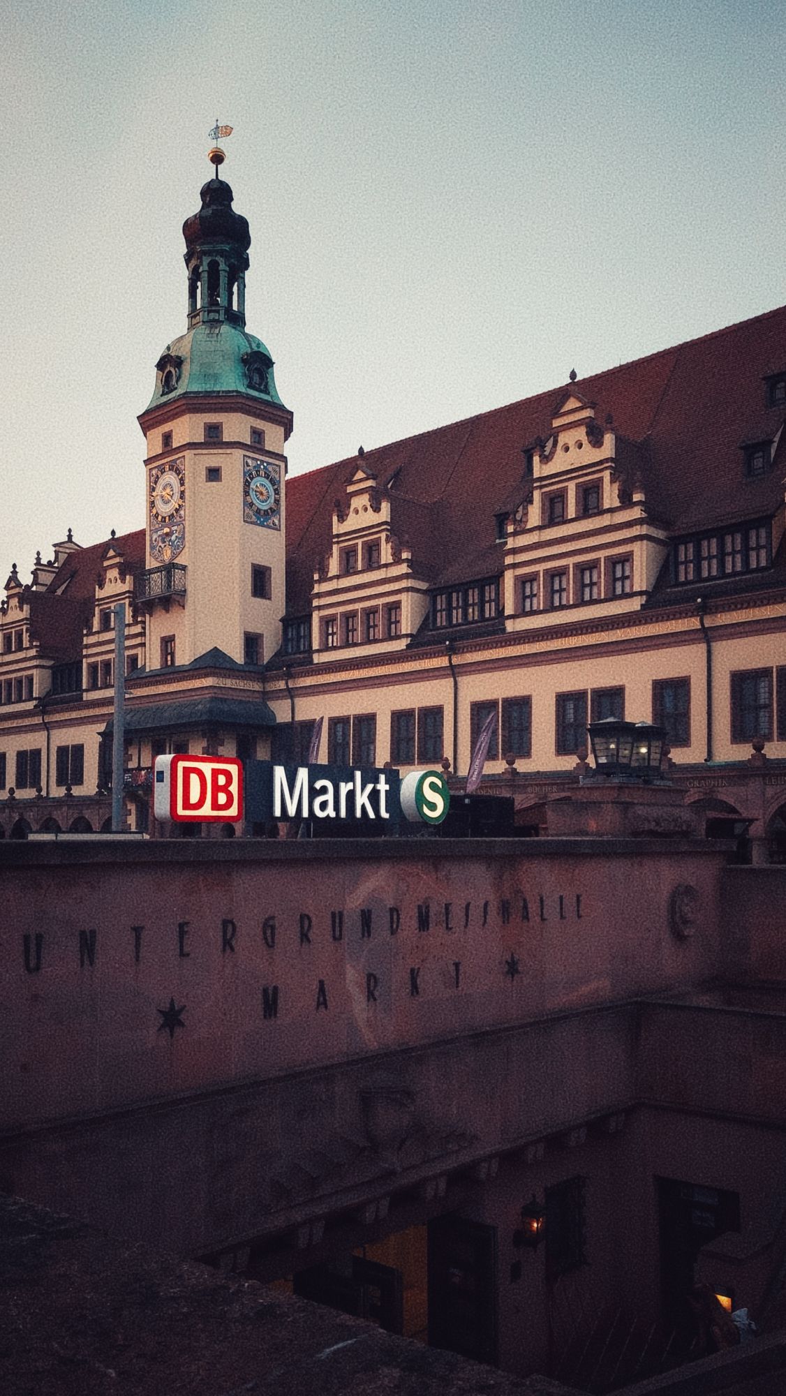 An old city building with a very unique facade and a tower. Entrance to a city train station in front. 