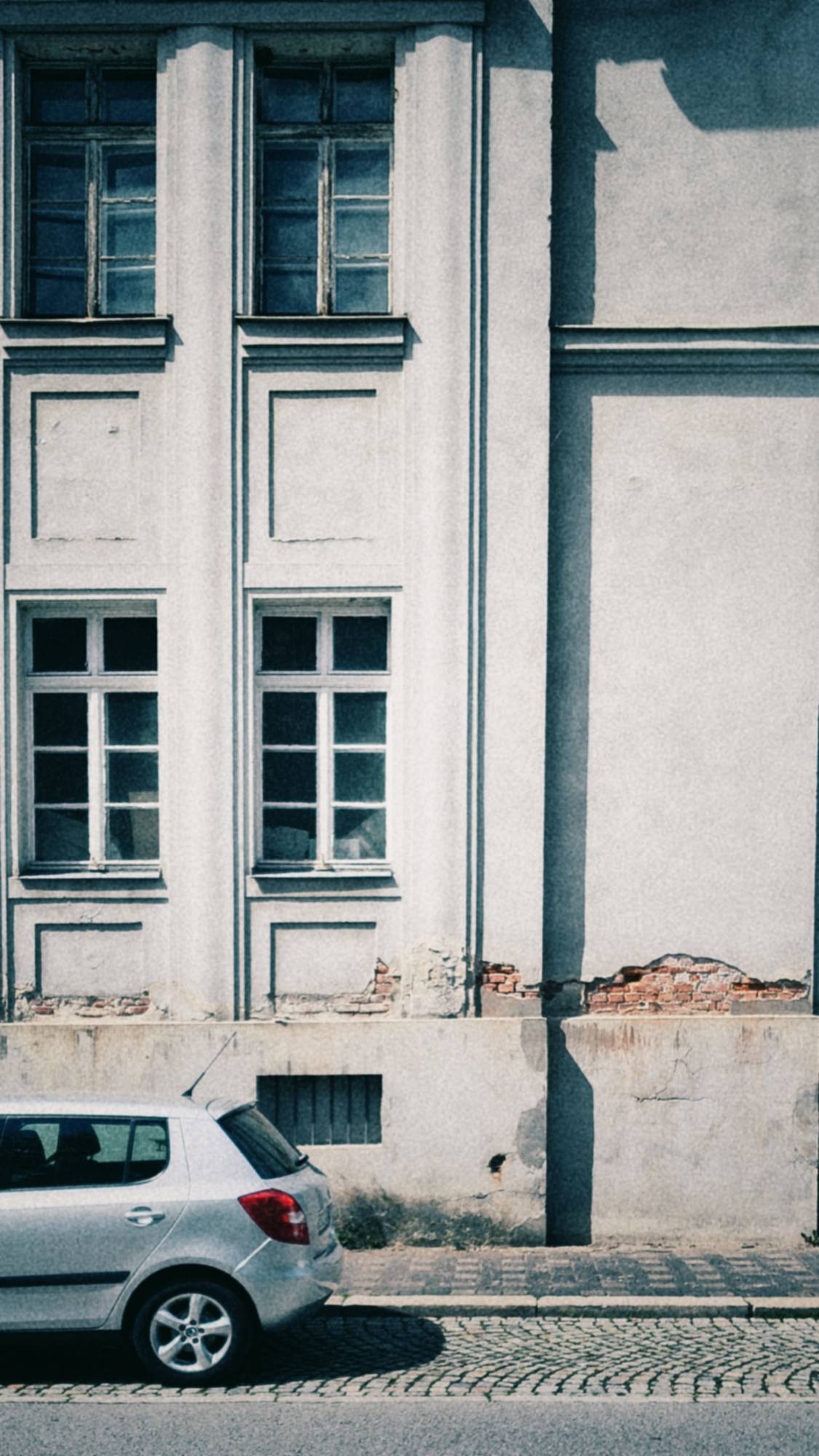 An old facade and a parked silver car in bright afternoon sun.