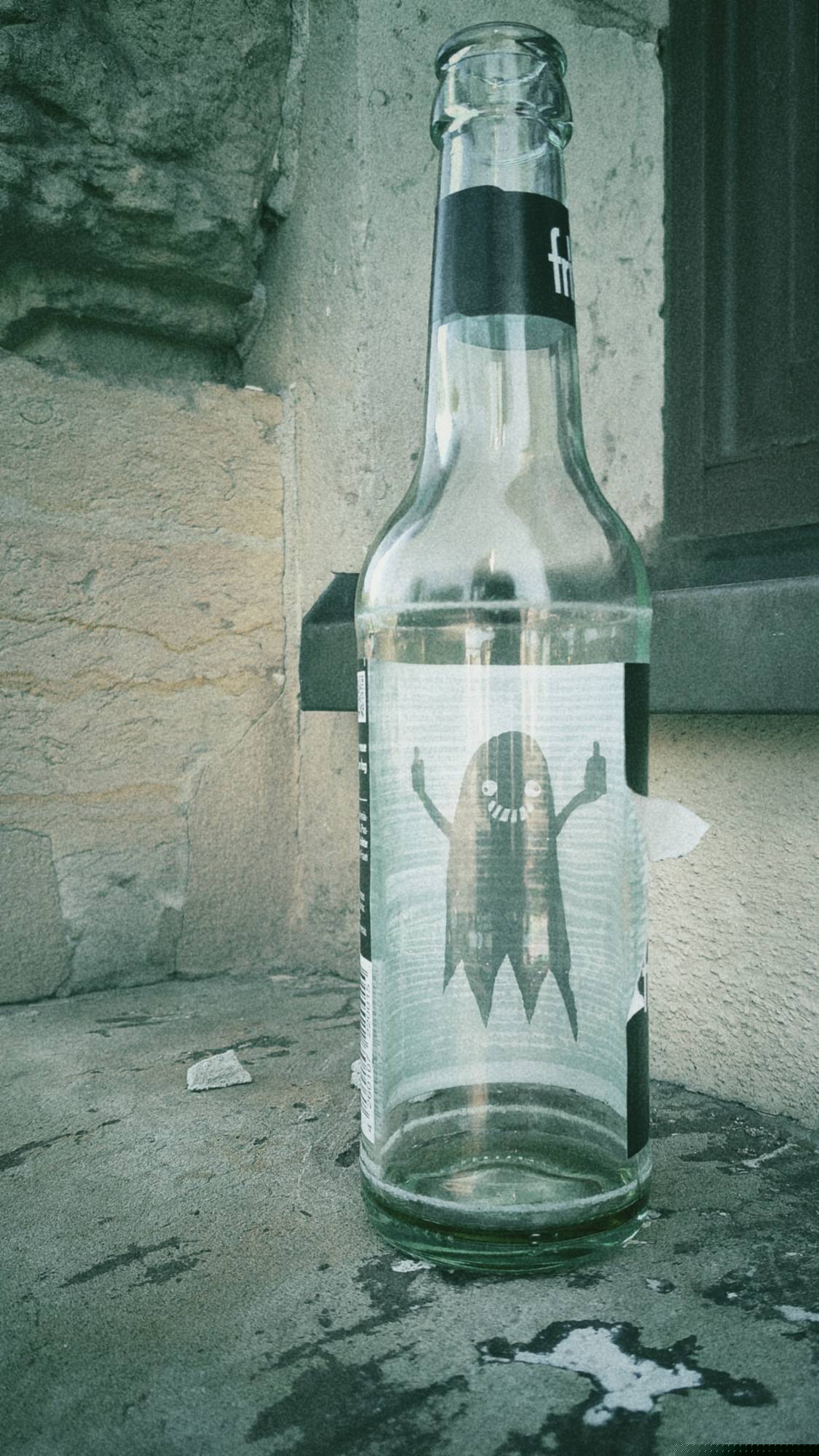 An empty Fritz Cola bottle on an old windowsill. The inner side of the label is white and has a black ghost on it. The ghost is grinning wide and has two middle fingers up.