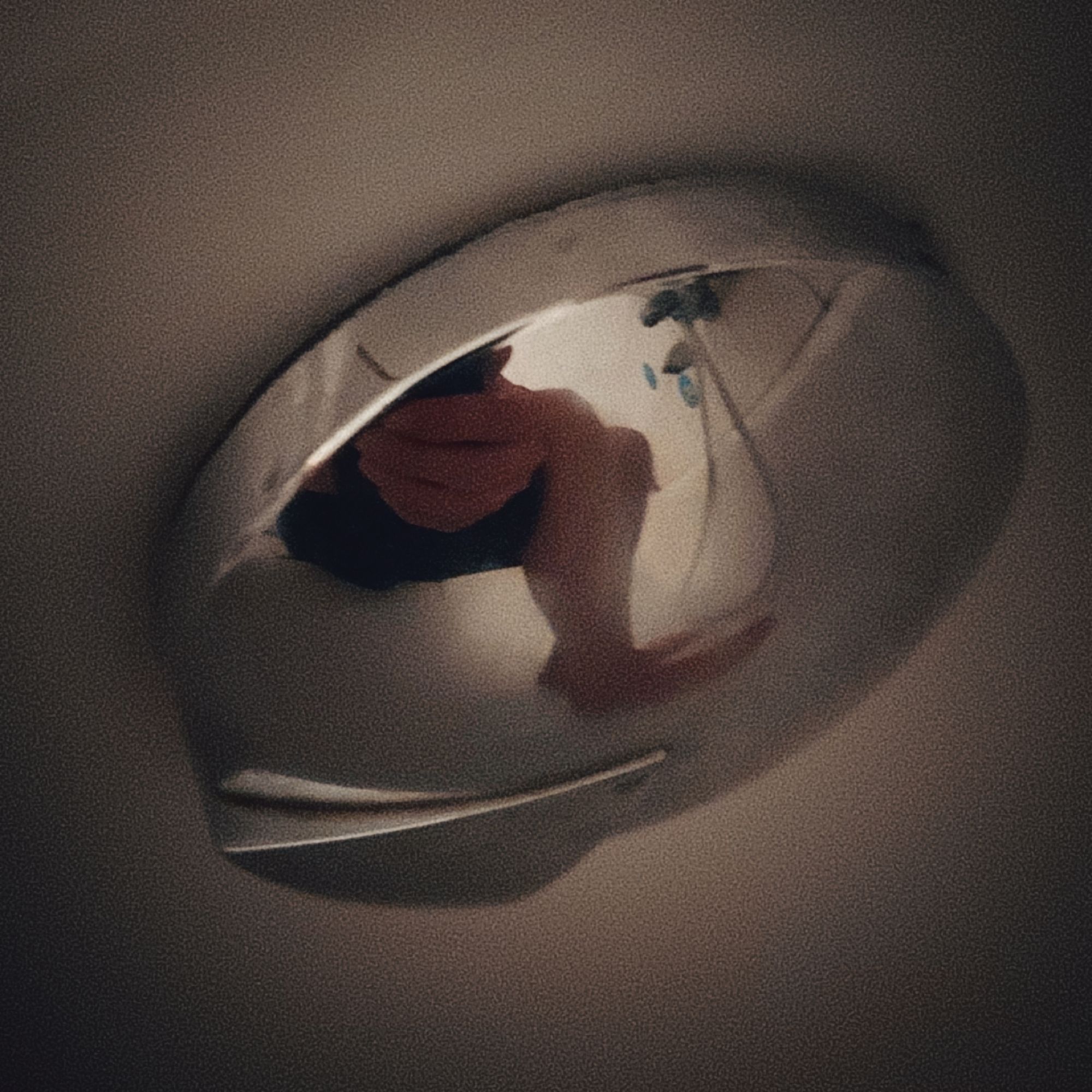 Legs in black shorts resting in cold water in a bathtub, reflected by a metal piece of plumbing.