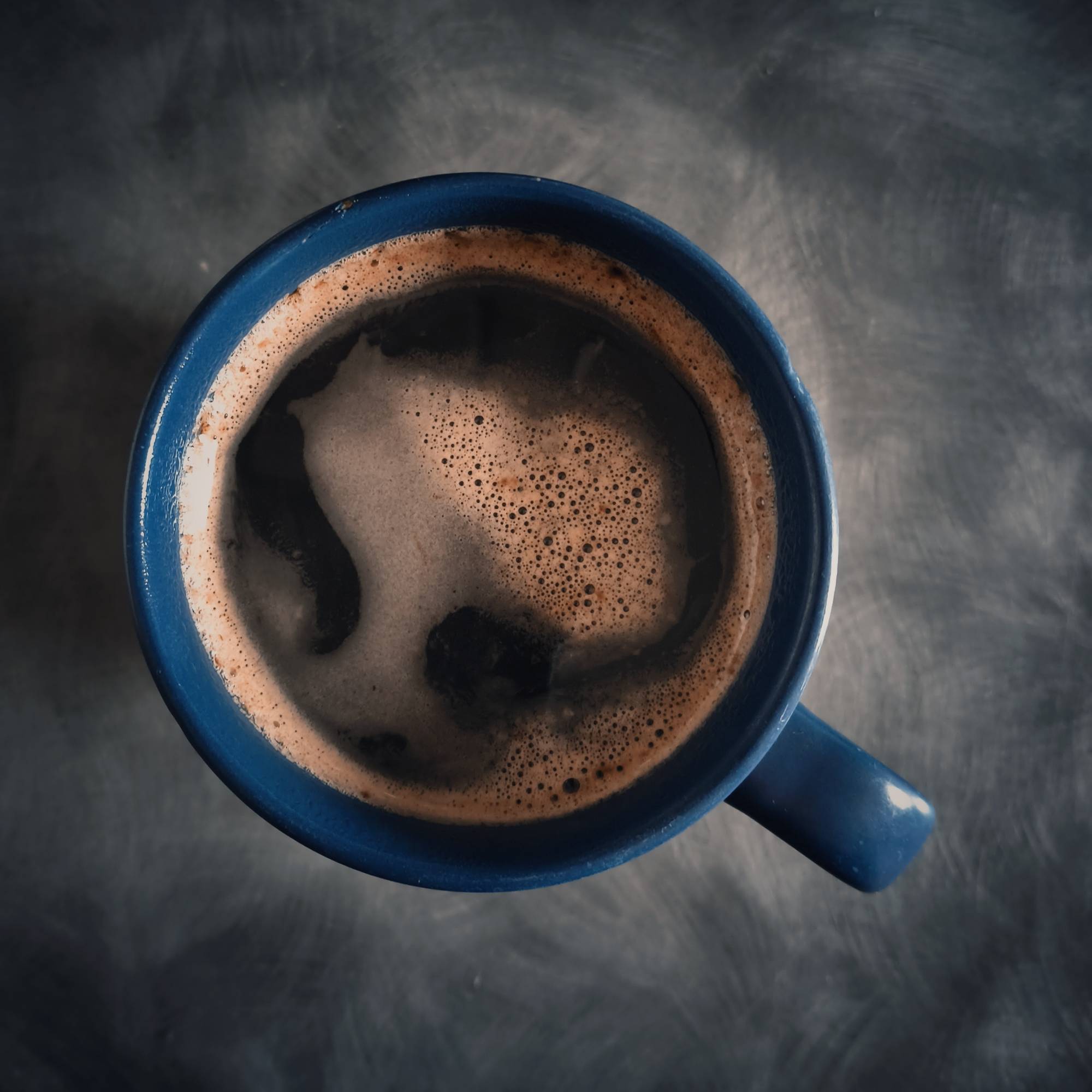 A blue mug containing black coffee, seen from above on a grey kitchen surface.